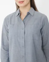 Camisa celeste de manga larga confeccionada en algodón chambray, con cuello clásico, cierre frontal con botones, dos bolsillos de parche en el pecho y corte relajado.