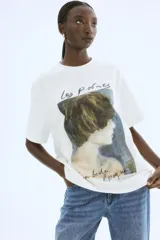 Remera color crudo de corte recto y mangas cortas, con estampado de una pintura de una mujer y texto en francés.