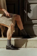 Mocasín de cuero color marrón con tachas metálicas plateadas en la puntera y laterales.