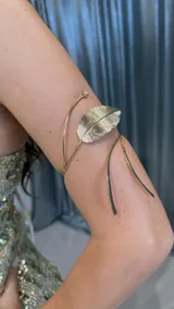 Brazalete dorado para el brazo, con forma de hoja y un pequeño brillante en un extremo.