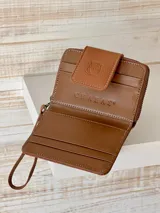 Billetera marrón de cuero con textura croco, cierre de cremallera y correa de muñeca. Presenta un broche con el logo de un búho.