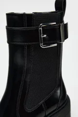 Botín negro estilo Chelsea con elástico lateral, hebilla decorativa y suela track con tacón bloque.