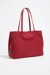 Bolso shopper grande de nylon color rojo, con estructura blanda y doble asa de hombro. Presenta un parche con el logo metálico de la marca en la parte frontal inferior.