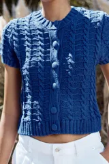 Chaqueta de punto azul con cuello redondo y manga corta. Cierre frontal con botones forrados y diseño en relieve.
