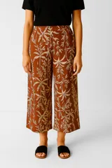 Pantalón holgado de tiro alto, corte ancho y largo hasta el tobillo, confeccionado en tela estampada con motivos botánicos en tonos terracota y beige.