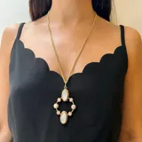 Collar con cadena de eslabones dorados y dije colgante de diseño geométrico en bronce. El dije presenta dos óvalos centrales de nácar y está rodeado por ocho cuentas pequeñas de perla o piedra blanca, engastadas en aros de bronce.