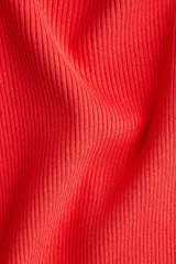 Top corto de punto acanalado color rojo, con escote amplio que deja los hombros descubiertos y un leve escote en V. Presenta mangas largas y un ribete fino de volados en los puños y el bajo.