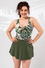 Vestido de baño enterizo con estampado de hojas de palmera en tonos verde, blanco y amarillo. Presenta escote redondo con nudo y abertura en el centro del busto, y falda corta verde oliva.