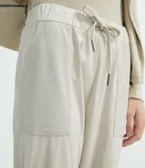 Pantalón jogger color beige, con elástico en la cintura y en los tobillos, cordón ajustable, bolsillos laterales y detalles de agujeros en los laterales y en los bolsillos.