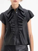 Camisa de cuero ovino negra, con volados en el centro delantero, mangas con volumen fruncidas en la copa y broches forrados en cuero.