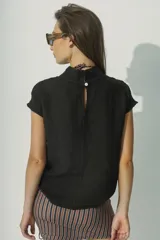 Blusa negra de lino con cuello alto y mangas cortas con detalle de calado en los hombros.