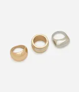 Set de tres anillos gruesos de metal con diferentes diseños: uno dorado liso, uno dorado con líneas plateadas y uno plateado con forma geométrica.