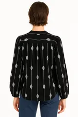 Blusa color crema con estampado de hojas color marrón, cuello mao con abertura y botones, mangas largas abullonadas con puños elásticos.