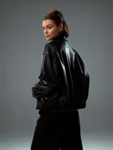 Chaqueta bomber negra de cuero sintético con cierre frontal y cuello clásico.