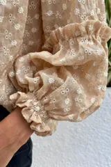 Camisa verde con rayas verticales blancas y bordados de flores. Tiene cuello mao, mangas largas abullonadas con puños elásticos y cierre frontal con botones de nácar.