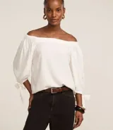 Blusa blanca de viscosa con escote off-shoulder y mangas 3/4 abullonadas con lazos en los puños.