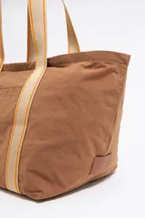 Bolso maxi de nylon color marrón con estructura blanda y doble asa de tejido con detalles en cuero. Incluye bolsillo interior, cierre con cremallera y placa metálica con logo grabado.