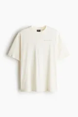 Remera color crema de corte holgado con cuello redondo y estampado pequeño en el pecho.