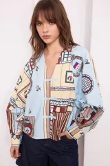 Camisa celeste con estampado de objetos y flores en tonos pastel, de manga larga y cuello en V con cierre de botones tipo alamar.