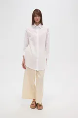 Camisa blanca de algodón con cuello clásico, corte holgado, cierre frontal con botones y mangas largas.