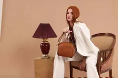 Bandolera de cuero sintético color beige, con diseño compacto y elegante. Cuenta con un bolsillo frontal con cierre y un compartimento principal con cierre. La correa es regulable.