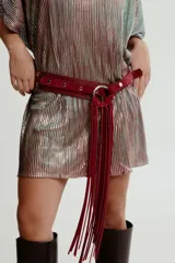 Cinturón de cuero color bordó con hebilla circular plateada y flecos largos.