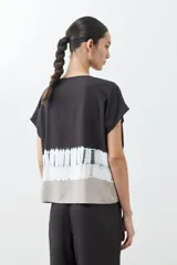 Blusa de manga corta con cuello redondo y cierre frontal parcial con botones. Presenta un diseño tie dye en tonos grises y blancos en la parte inferior.