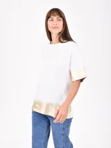 Remera blanca de corte holgado con mangas cortas y estampado dorado en el frente y en los bordes.