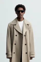 Trench largo regular fit color beige confeccionado en tejido italiano repelente al agua. Tiene cuello con solapas de pico, manga larga con puño ajustable con trabilla, bolsillos de vivo en cadera, bolsillo interior, cinturón del mismo tejido en cintura, bajo con abertura en centro espalda y cierre frontal de botonadura cruzada.