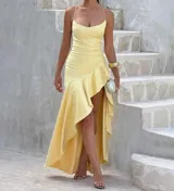 Vestido largo color amarillo claro, con escote drapeado, tirantes finos y falda asimétrica con volados y abertura lateral.
