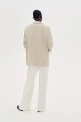 Blazer color beige de corte recto, con solapas de pico, bolsillos delanteros con solapa y mangas con forro a rayas.