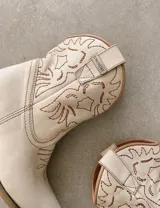 Botas cortas negras de cuero con bordados blancos estilo cowboy.