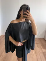 Conjunto negro brillante compuesto por un top corto con escote off-shoulder y mangas anchas, y una falda corta con lazo lateral.