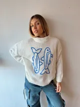Sweater de punto color crema con cuello alto y estampado de dos peces azules en el frente.