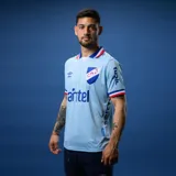Camiseta de fútbol Umbro del Club Nacional de Football, modelo Away 3. Diseño celeste con detalles en azul y rojo en cuello y mangas. Incluye logo de Umbro, escudo del club y sponsors.