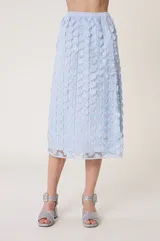 Falda midi de tul celeste bordada con flores y lentejuelas. Tiene forro de tejido tipo cuadros vichy con calados transparentes, cintura elástica y corte recto, ligeramente acampanado en el bajo.