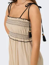 Vestido midi color arena con tirantes finos ajustables y detalle de borlas negras. Presenta un diseño smock en el corpiño y falda con caída fluida.