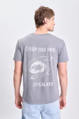 Remera de manga corta color gris con efecto lavado, con estampado en la espalda que incluye una galaxia espiral y texto que dice "Create your own" y "/// GALAXY".