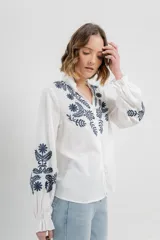 Camisa de manga larga en algodón liviano, color azul marino, con bordados florales en contraste en el frente y mangas. Cuello mao con terminación en ondas y puños fruncidos.