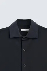 Camisa color beige de corte slim fit, confeccionada en tejido elástico que minimiza las arrugas. Tiene cuello italiano abierto, manga larga con puños abotonados y cierre frontal con botones.