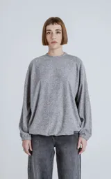 Sweater gris jaspeado de manga larga y cuello redondo, con elástico ajustable en el ruedo inferior.