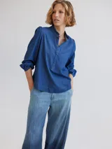 Camisa de denim azul con cuello mao con volados, mangas largas abullonadas con puños elásticos y cierre frontal con botones. Corte semi entallado.