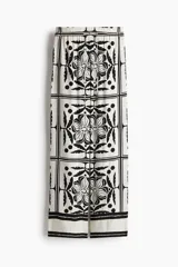 Pantalón largo de viscosa color blanco con estampado de flores y figuras geométricas en negro. Tiene tiro alto, cintura elástica con cordón ajustable, bolsillos laterales y corte holgado.