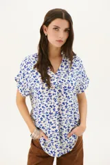 Blusa estampada con hojas azules sobre fondo blanco, con cuello en V y mangas cortas con dobladillo.