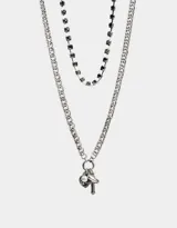 Set de dos collares plateados de diferentes largos, uno con cadena gruesa y dijes de corazón, cruz y perla, y otro con cadena de strass negros.