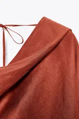 Blusa color ladrillo confeccionada en lino 100%. Tiene cuello fluido, mangas largas acampanadas y espalda descubierta ajustable con cordones.