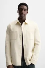Sobrecamisa negra de tejido con elasticidad, cuello solapa y manga larga acabada en puño con botón a presión. Tiene bolsillos de plastrón en el pecho y cierre frontal con botones a presión.