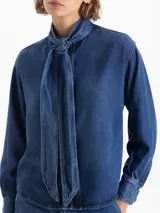 Camisa azul de manga larga confeccionada en 100% Tencel, con lazo en el cuello y acceso mediante broches dorados en la cartera delantera.