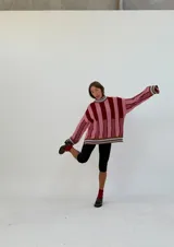 Buzo de punto oversize con cuello alto y mangas largas. Diseño a rayas verticales en tonos rosa y borgoña, con detalles en marrón y celeste en cuello, puños y ruedo.