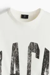 Musculosa blanca de algodón con cuello redondo y sisas sin rematar. Estampado negro con la palabra 'L.A.C.A' en el frente. Corte holgado.